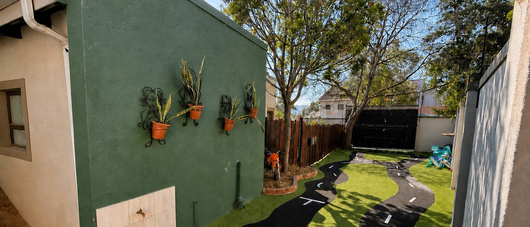Greenhill se buitespeelarea met die groen muur, potplante en die fietsbaan