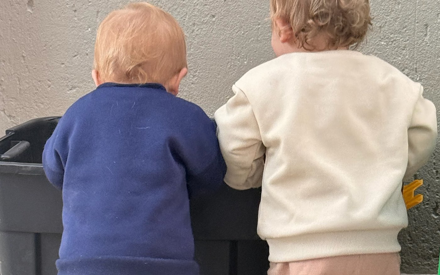 Twee peuters wat langs mekaar by 'n houer saam speel